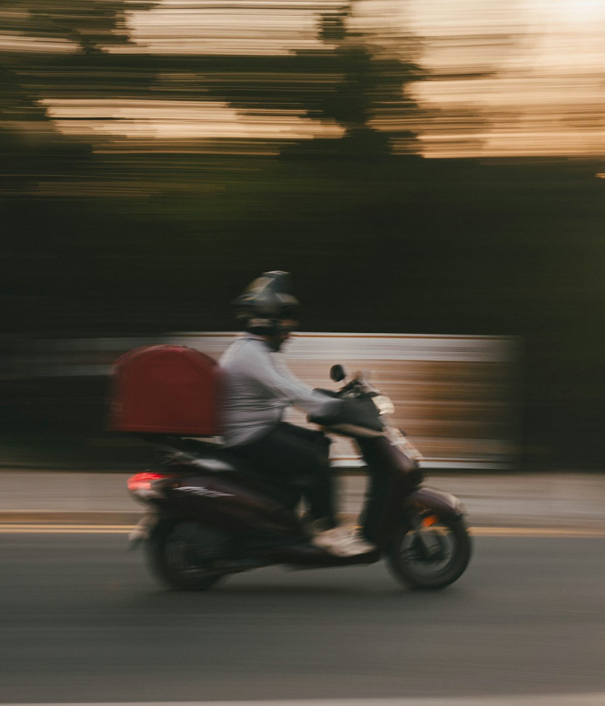 Livreur en scooter avec un coffre de livraison, en fin de journée